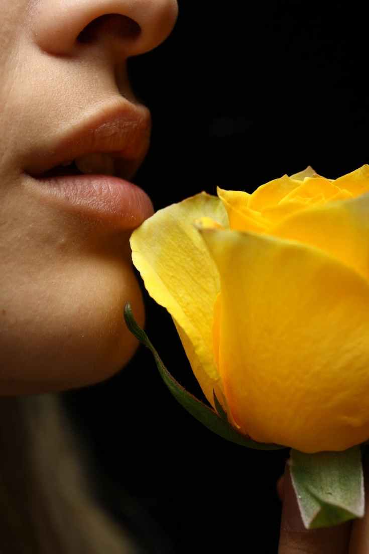 selective focus photography of woman smelling yellow rose flower